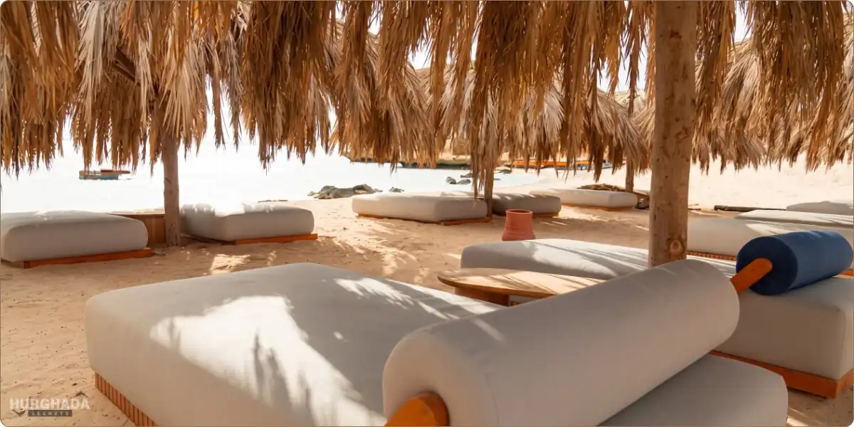 Comfortable white sunbeds shaded by traditional straw umbrellas on the sandy beach of Ozirea Island in Hurghada.