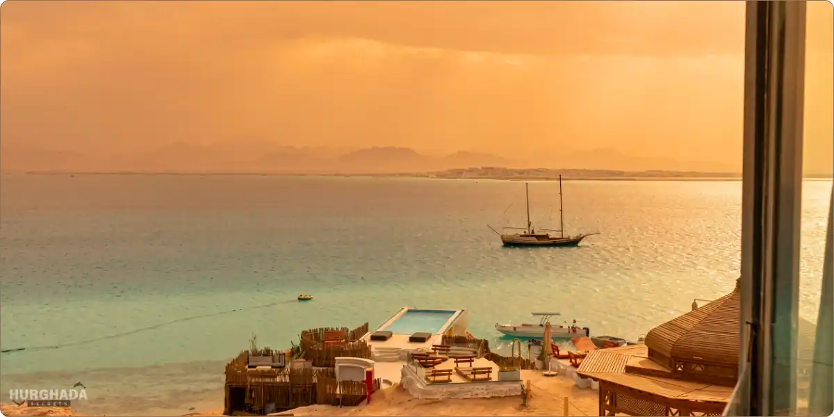 Stunning sunset view over Ozirea Island in Hurghada, showing the golden sky reflecting on the Red Sea with a sailing boat and luxury beach facilities.