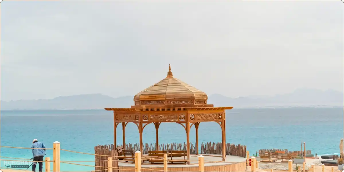 An elegant wooden oriental gazebo on a high point of Ozirea Island in Hurghada, overlooking the turquoise waters of the Red Sea and distant mountains.